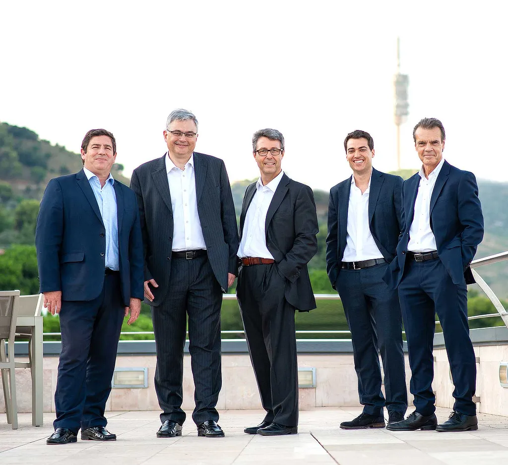 Grupo de cinco profesionales vestidos con traje posando en exterior con paisaje urbano de fondo, representando al equipo directivo de Atlantis una compañía especializada en inversión y gestión estratégica.