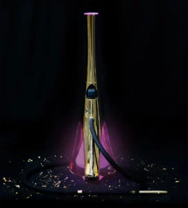 Shisha dorada con base iluminada en tonos violetas sobre fondo oscuro, acompañada de detalles decorativos dorados que refuerzan su carácter premium y su estilo minimalista.