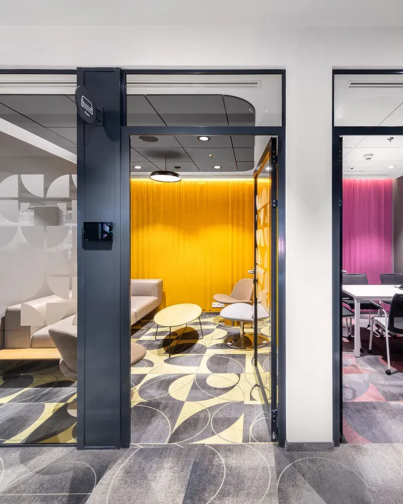 Oficinas con varias salas acristaladas que combinan cortinas amarillas y magenta, mobiliario de líneas suaves y suelos con diseños geométricos en tonos neutros.