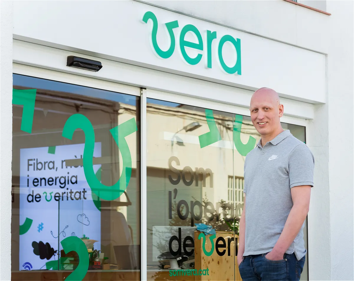 Fachada de una tienda Vera con cristaleras decoradas, logotipo visible y un hombre posando sonriente delante, representando la presencia física de la marca.